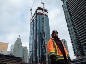 Mathew Tiburcio poses for a portrait after his shift operating a crane, seen in the background, high above even some of the tallest downtown buildings as construction continues on CIBC Square in Toronto.