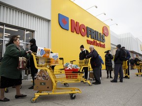 A shopper pushes a cart filled with paper towels and supplies as others wait in line to enter a No Frills supermarket in Toronto, Ontario, Canada on Saturday, March 14, 2020.