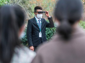 This photo taken on March 24, 2020 shows a security guard (C) wearing an augmented reality (AR) headset used to measure a visitor's body temperature at a park in Hangzhou in China's eastern Zhejiang province.