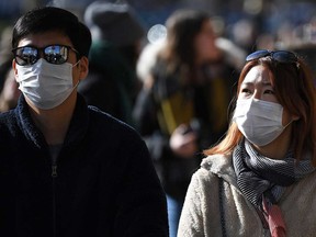 Tourists wearing surgical face masks walk in Westminster in central London on Monday. - Britain's Prime Minister Prime Minister on Monday chaired an emergency COBRA meeting on the coronavirus outbreak, after the number of confirmed cases of COVID-19 in the United Kingdom rose to 36.