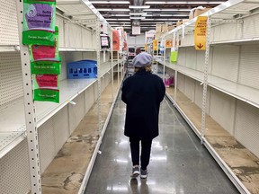 A shopper walks past empty shelves normally stocked with soaps, sanitizers, paper towels, and toilet paper at a grocery store in California.