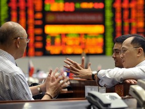 Traders chat in front of  an electronic index board.