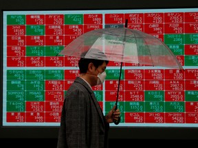 A visitor wearing protective face mask, following an outbreak of the coronavirus, walks past in front of a stock quotation board outside a brokerage in Tokyo, Japan on Monday.