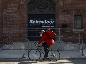 A food delivery courier wearing a protective mask bikes down Queen St. in Toronto, on March 25, 2020.