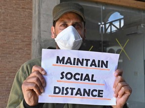 A policeman wearing a facemask holds a sign as Bangladeshi medical students return home after completing 14-days of quarantine during government-imposed nationwide lockdown as a preventive measures against the spread of the COVID-19 coronavirus on April 2, 2020.