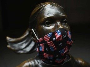 The "Fearless Girl" statue wears a face mask with American Flags outside the New York Stock Exchange.