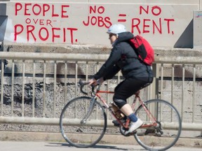 A cyclist rides past graffiti stating "People Over Profit No Jobs = No Rent in Toronto during the Covid 19 pandemic. More than 7.1 million Canadian residents have applied for the $2,000 monthly Canada Employment Response Benefit since April 6.