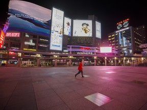 A pedestrian crosses a nearly empty Dundas Square in Toronto, in late March 2020.