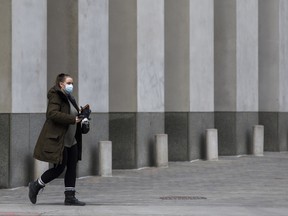 pedestrian wearing a protective mask walks on Queen St. in Toronto.