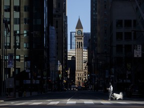 pedestrian crosses the street with a dog during morning commuting hours in Toronto's financial district amid a shutdown due to the coronavirus.