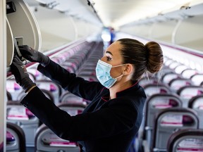 A member of the cabin crew wearing a protective face mask places an item into the overhead baggage hold ahead of the flight on-board a passenger aircraft operated by Wizz Air Holdings Plc at Liszt Ferenc airport in Budapest, Hungary, on Monday, May 25, 2020.