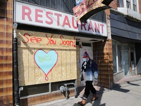 A man wearing a protective face mask passes a boarded-up restaurant during the global outbreak of the coronavirus disease in Toronto.