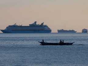 Fishermen sail past a group of cruise ships anchored in Manila Bay on May 8 as its crew members undergo quarantine amid the coronavirus outbreak.