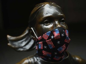 The "Fearless Girl" statue wears a face mask with American Flags outside the New York Stock Exchange.
