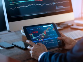 Businessman checking stock market on digital tablet and a desktop computer with stock exchange graph on screen. Financial stock market. Analyzing data in office background.