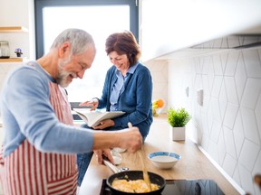 A portrait of senior couple in love indoors at home, cooking.