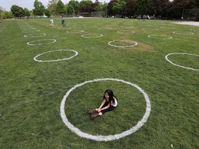 A girl sits in a field where circles were painted to help visitors maintain social distancing at Trinity Bellwoods park in Toronto.