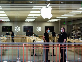 Employees wearing protective masks stand outside an Apple store in Syracuse, New York.