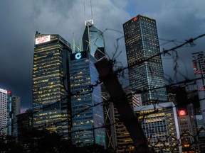 A barbed-wire fence stands near buildings illuminated at dusk in the Central district in Hong Kong, China.