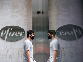 A pedestrian wearing a protective mask passing in front of Pfizer Inc. signage is reflected outside the company's headquarters in New York, U.S., on Wednesday, July 22, 2020.