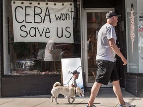A pedestrian walks his dog walks in June past a store on Toronto’s Dundas Street West stating CEBA Won’t Help Us during the COVID-19 pandemic.