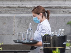 A server wears a face mask as she carries a tray of glasses and water at a restaurant in Montreal, Sunday, July 5, 2020.