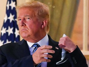 U.S. President Donald Trump pulls off his protective face mask as he poses atop the Truman Balcony of the White House after returning from being hospitalized for coronavirus disease treatment this past week.