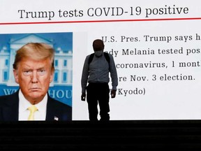 A man wearing a protective mask in Tokyo amid the coronavirus disease outbreak, walks past a large screen showing a news about U.S. President Donald Trump who is tested positive for COVID-19.