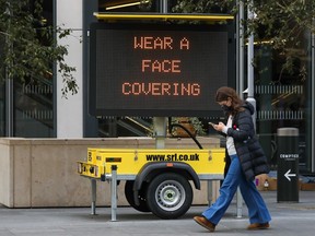 A pedestrian wearing a protective face mask passes a matrix sign displaying a message that reads "Wear A Face Covering" in London, U.K., on Thursday, Oct. 15, 2020.