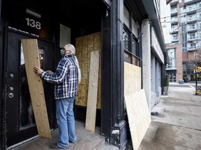 A person wearing a protective mask boards up his bar in downtown Toronto. The city will announce new restrictions on businesses early next week in an effort to slow the spread of the novel coronavirus.