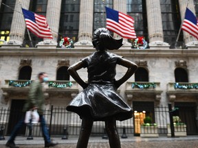 People walk past the New York Stock exchange (NYSE) and 'Fearless Girl' statue on Wall Street.