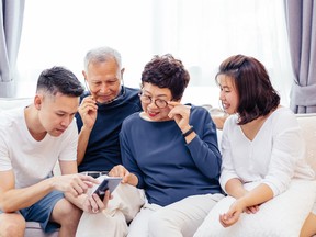 Asian family with adult children and senior parents using a mobile phone and relaxing on a sofa at home together
