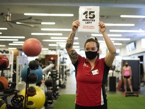 A staff member wearing a protective mask holds up a sign indicating the remaining time for members to complete their workouts before they must leave to allow staff to complete a 30- minute cleaning regimen at a GoodLife Fitness Centers Inc. gym in Ottawa this past summer.