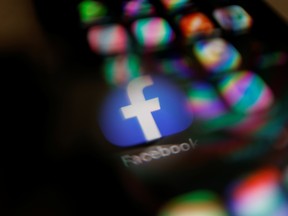 The Facebook logo displayed on a mobile phone seen through a magnifying glass.