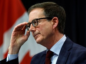 Bank of Canada Governor Tiff Macklem adjusts his glasses at a news conference. Behind him is the Canadian flag..