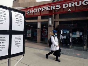 A woman wearing a face mask walks past a Shoppers Drug Mart store advertising coronavirus vaccines, in Toronto. Despite a second lockdown, the economy showed surprising strength.