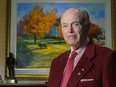 Jim Pattison wearing a red suit in front of a painting of an autumn scene.