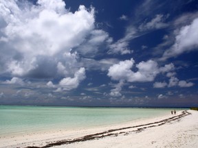 Two people walking in the distance on the beach of a private island.
