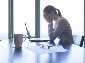 A woman holding her face in her hands in front of a laptop computer in an office.