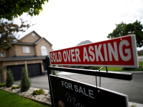 A real estate sign that reads For Sale and Sold Above Asking stands in front of housing in Vaughan, a suburb of Toronto.