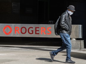 A pedestrian wearing a mask walks past Rogers signage at the company's head office in Toronto.