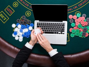 A close up of poker player with playing cards, laptop and chips at green casino table.