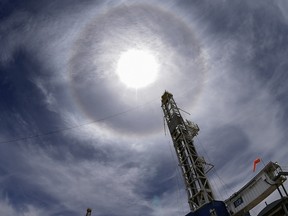 A natural gas drilling rig set against the sun and a blue sky.