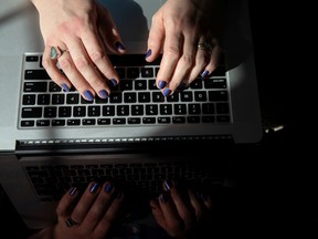 A woman's hands with purple nail polish working on a laptop.