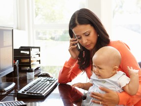 A mother with a baby on her lap working in a home office while on the phone.