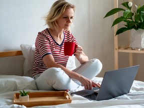 A woman working from her bed, holding a red coffee cup.