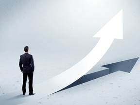 A young adult salesman standing in front of a big arrow pointing up with a shadow in grey empty space concept.