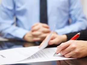 A woman signing a contract with a red pen with a businessman in the background