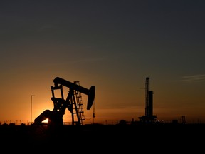 A pump jack operates in front of a drilling rig at sunset in an oil field in Midland, Texas.
