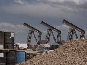 A line of pumpjacks next to stacked oil barrels